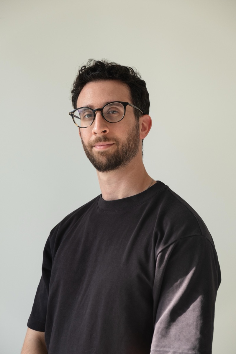 Bassam Huneidi in a black T-shirt against a plain wall.